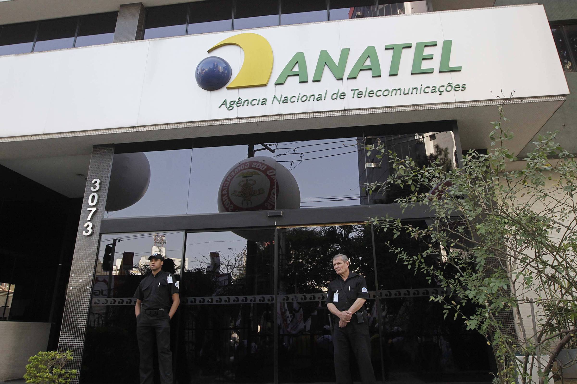 A imagem mostra a fachada da sede da ANATEL (Agência Nacional de Telecomunicações) em um edifício. O logotipo da ANATEL é visível na parte superior, com as palavras
