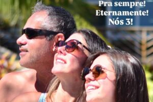 Três pessoas estão posando para a foto ao ar livre, sorrindo e olhando para o horizonte. Eles estão usando óculos de sol e roupas de banho coloridas. O fundo é de um ambiente tropical, com palmeiras visíveis. Há um texto na parte superior que diz: