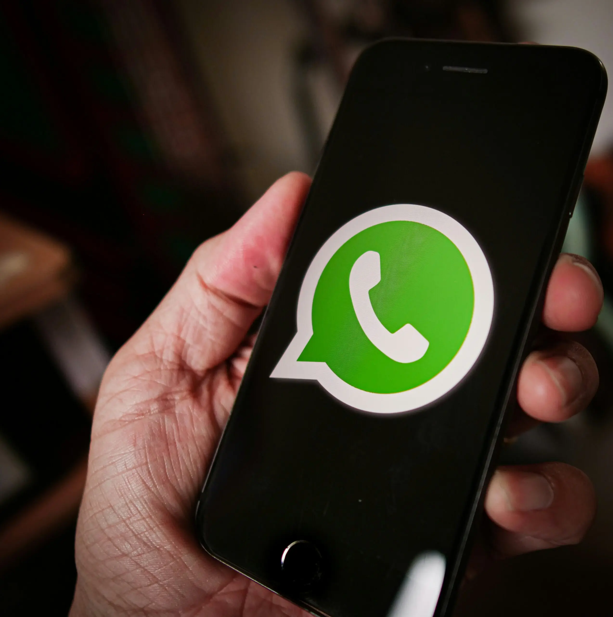 Pessoa segurando um celular aberto na página inicial do WhatsApp.