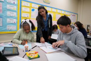 Teacher standing between two seated students in class.