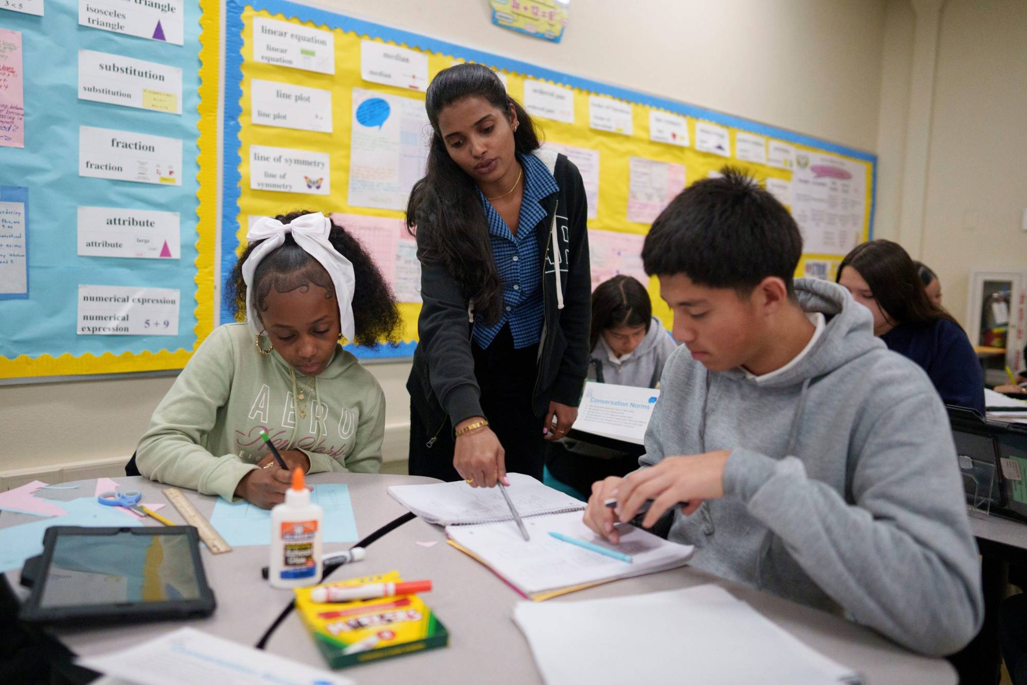 Teacher standing between two seated students in class.