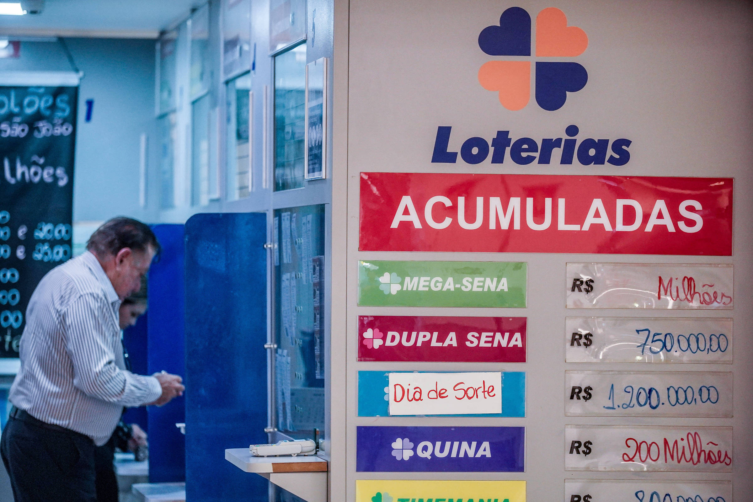 A imagem mostra um ambiente de loteria, com um homem em pé ao lado de um balcão. Na parede, há um cartaz grande com a palavra