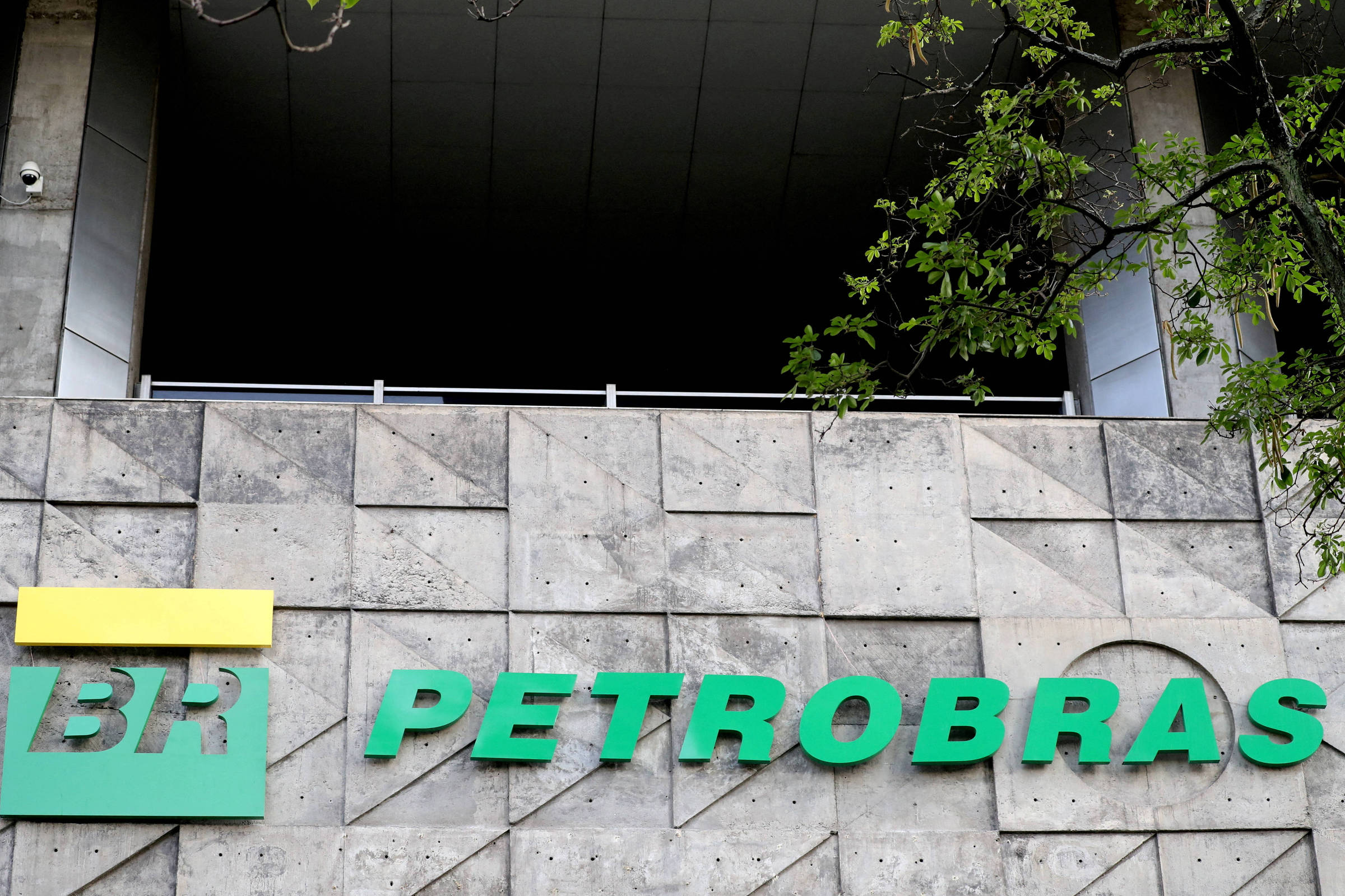 A imagem mostra o logotipo da Petrobras em uma parede de concreto. O logotipo é composto por um retângulo amarelo com as letras