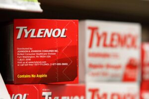 A imagem mostra uma caixa de Tylenol, um medicamento analgésico, em uma prateleira de farmácia. A caixa é predominantemente vermelha com o nome