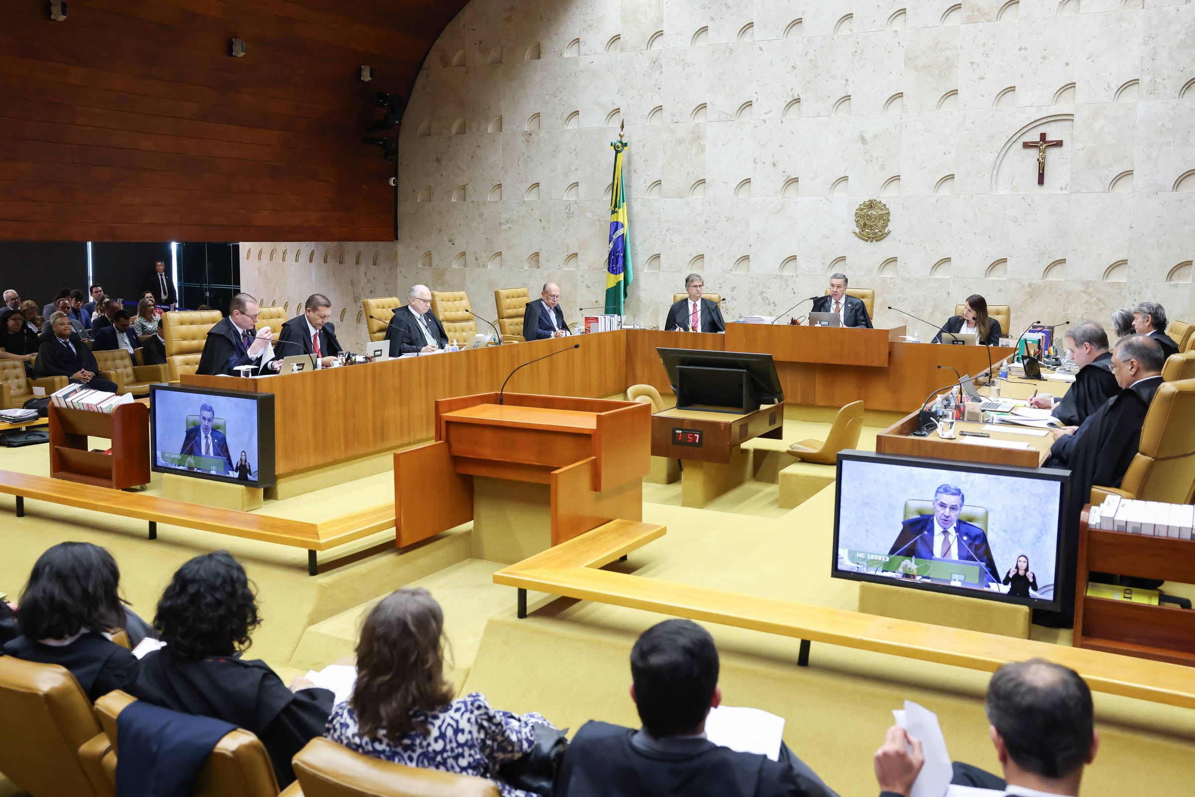 Imagem aberta de plenário do tribunal, com juízes posicionados e um crucifixo ao fundo