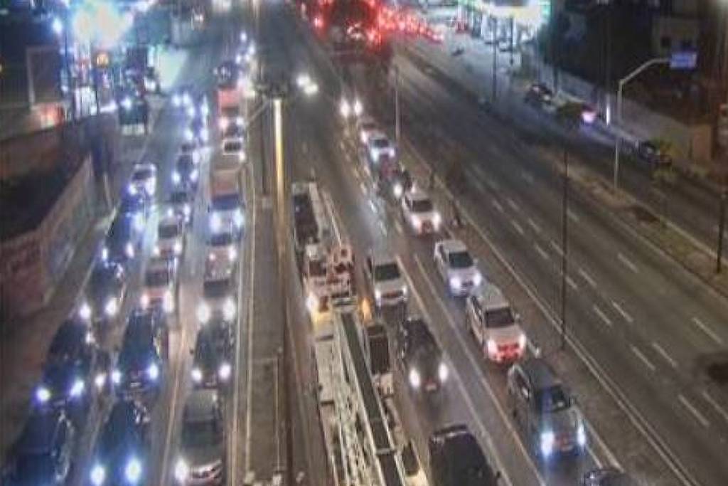 Marginal Pinheiros com tráfego intenso em ambas as direções durante a noite. Veículos com faróis acesos formam filas nas faixas centrais e laterais. Luzes de prédios ao fundo indicam área urbana.