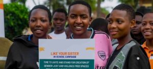 Três garotas sorridentes segurando um cartaz para a campanha "Like Your Sister" nas escolas, defendendo espaços sem violência e justiça de gênero nas escolas.
