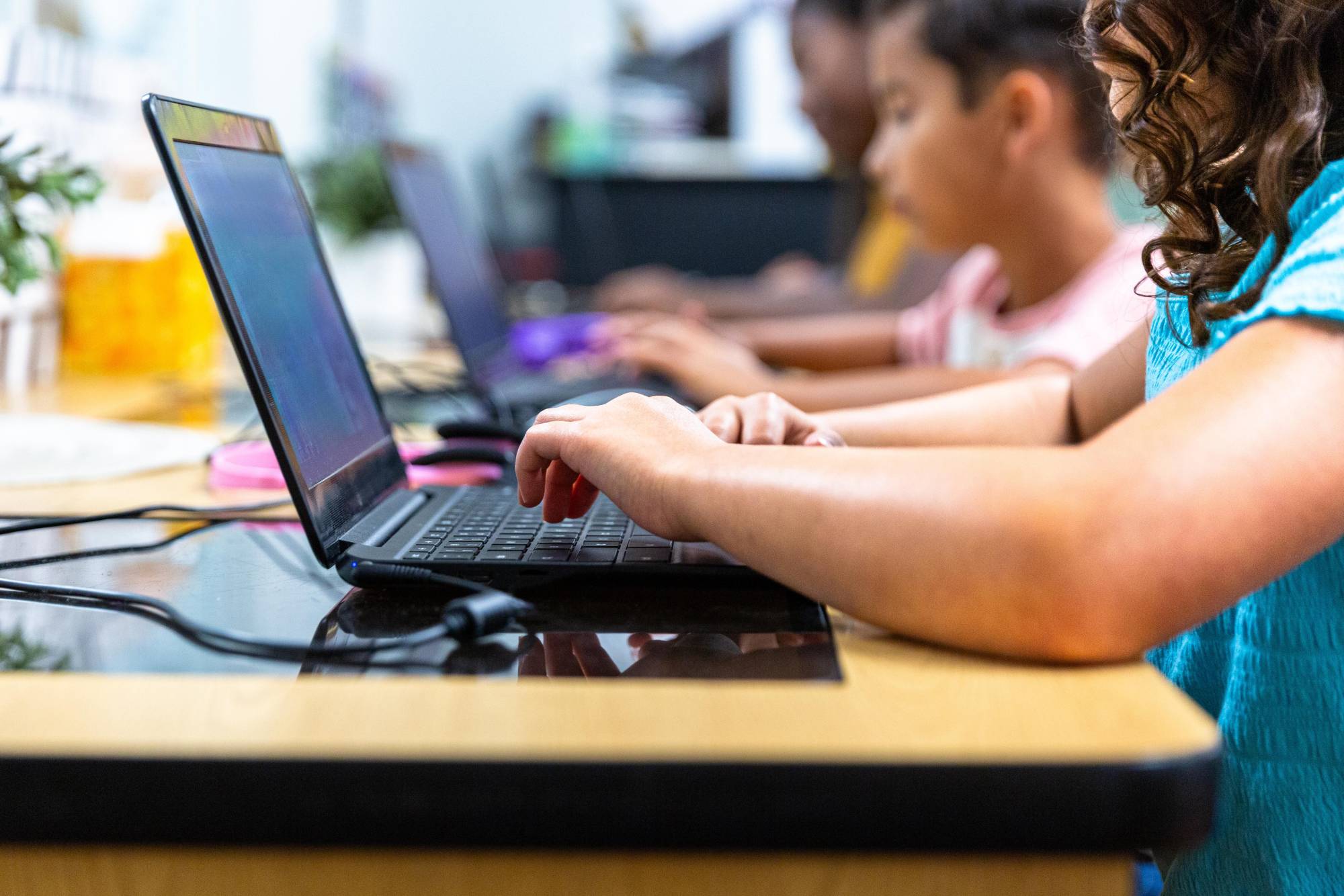 A stock photo shows elementary school students working on laptops.