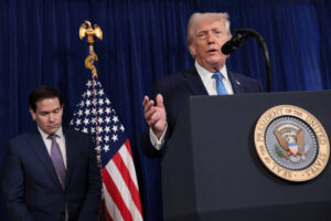 Ex-presidente dos Estados Unidos fala em púlpito com selo presidencial, enquanto senador está ao lado com olhar para baixo. Bandeira americana e cortina azul ao fundo.