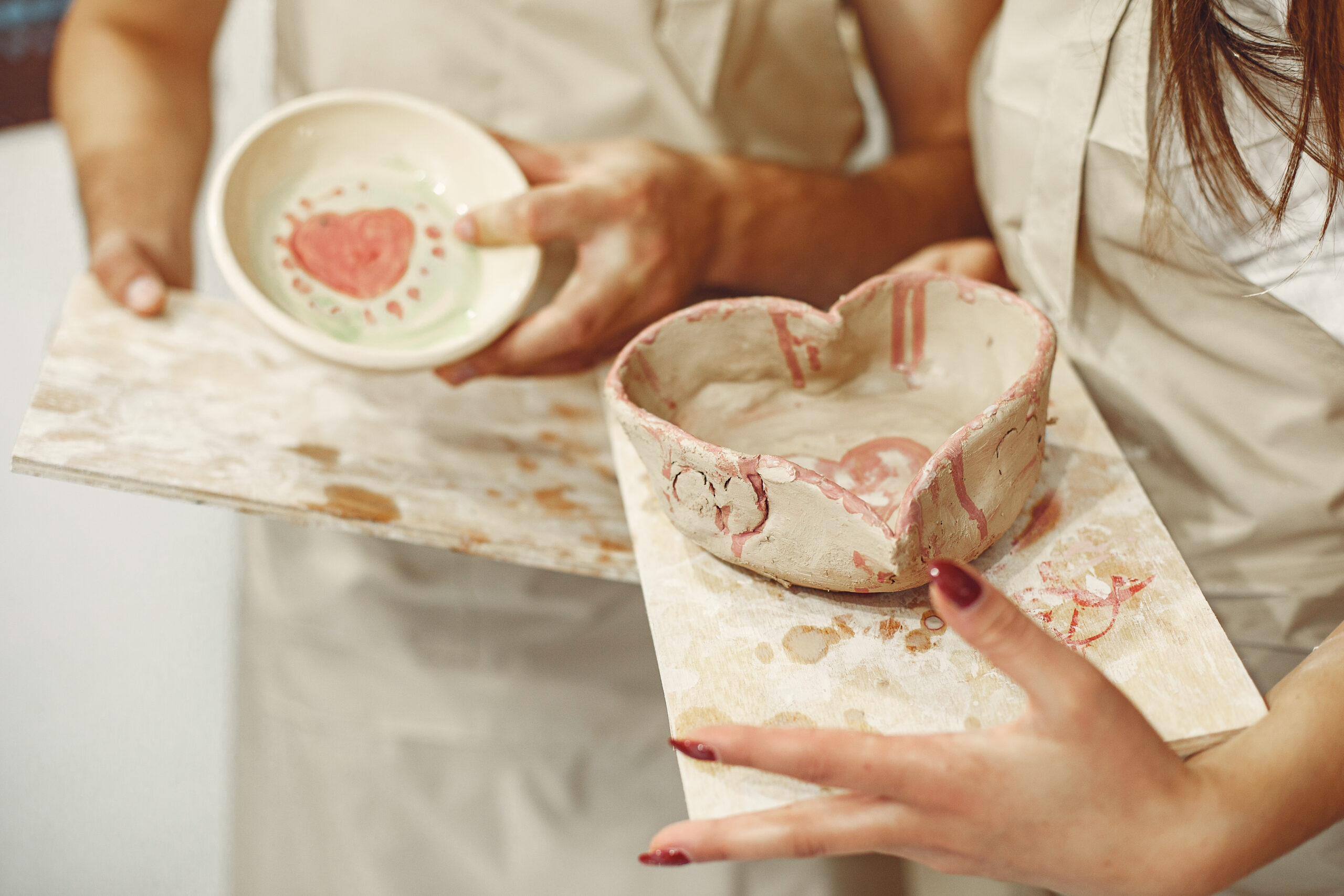 Mutual creative work. Young beautiful couple in casual clothes and aprons. People holds ceramic dishes.