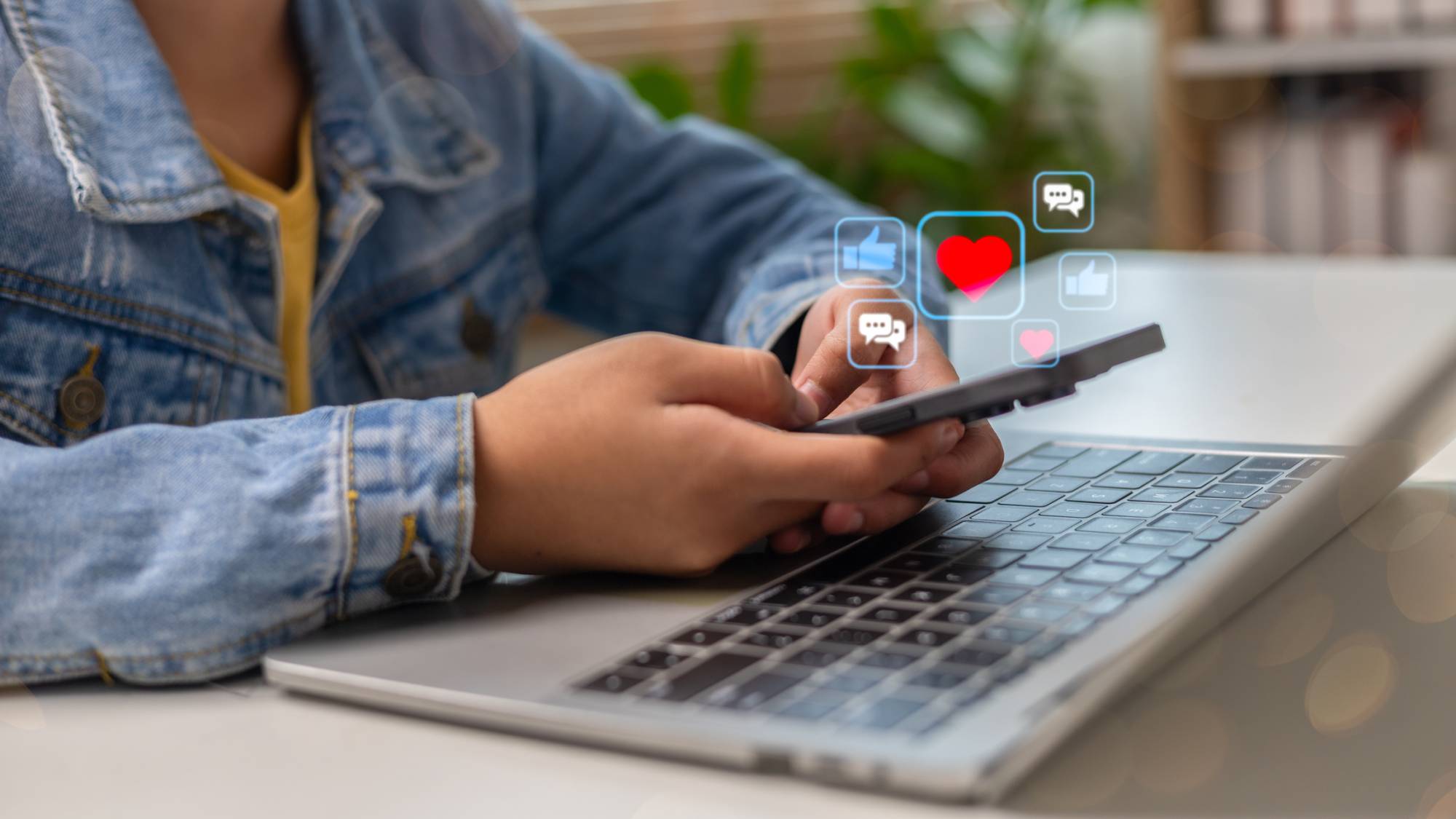 Teen scrolls on phone while working on laptop