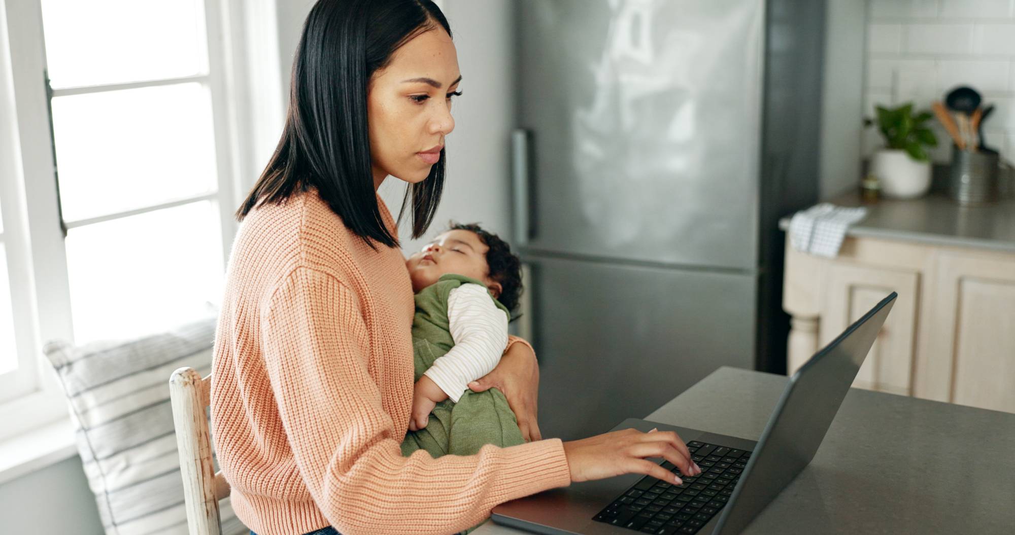 Mother, baby and laptop in kitchen for remote work.