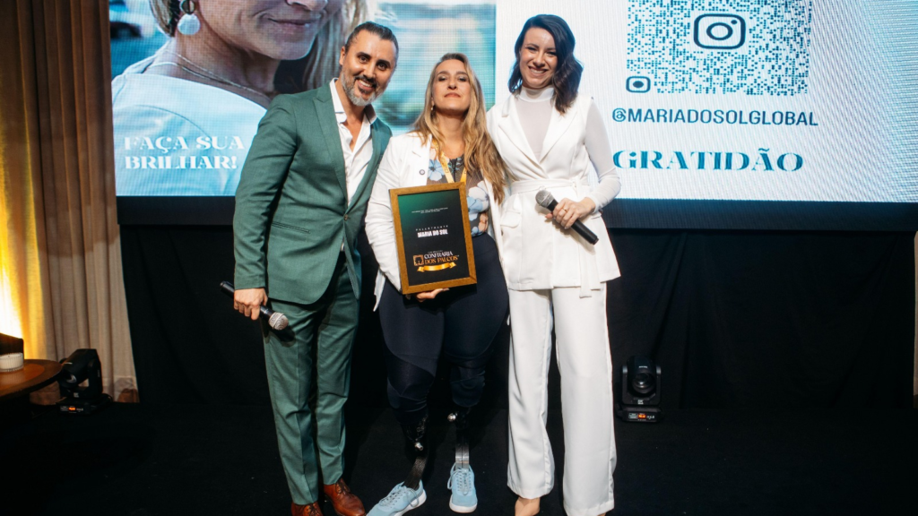 Maria do Sol no palco da Confraria dos Palcos recebendo reconhecimento ao lado de Fernando Freitas e Bruna Grah