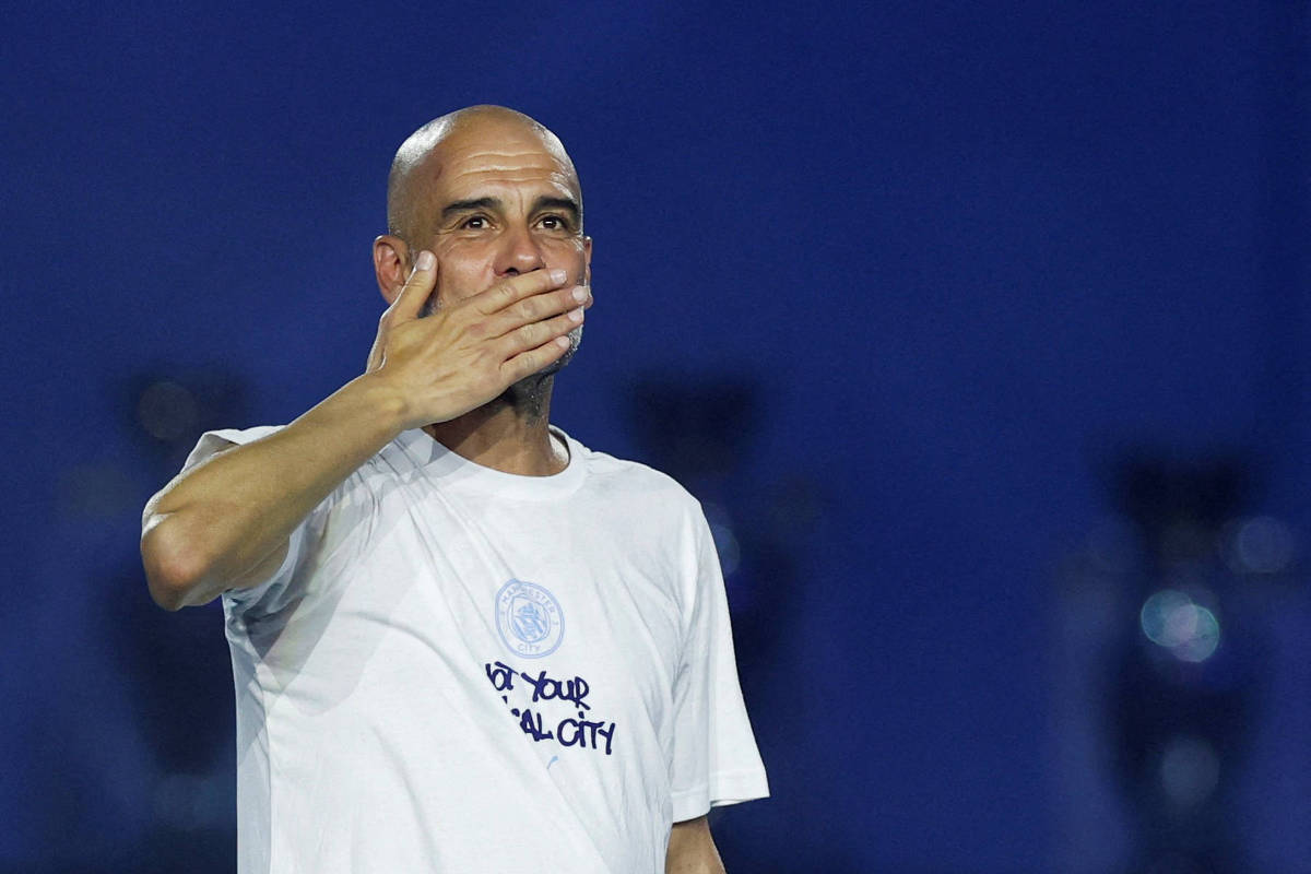 Homem careca com camiseta branca com texto parcialmente visível, gesto de mão cobrindo a boca, fundo azul escuro desfocado.